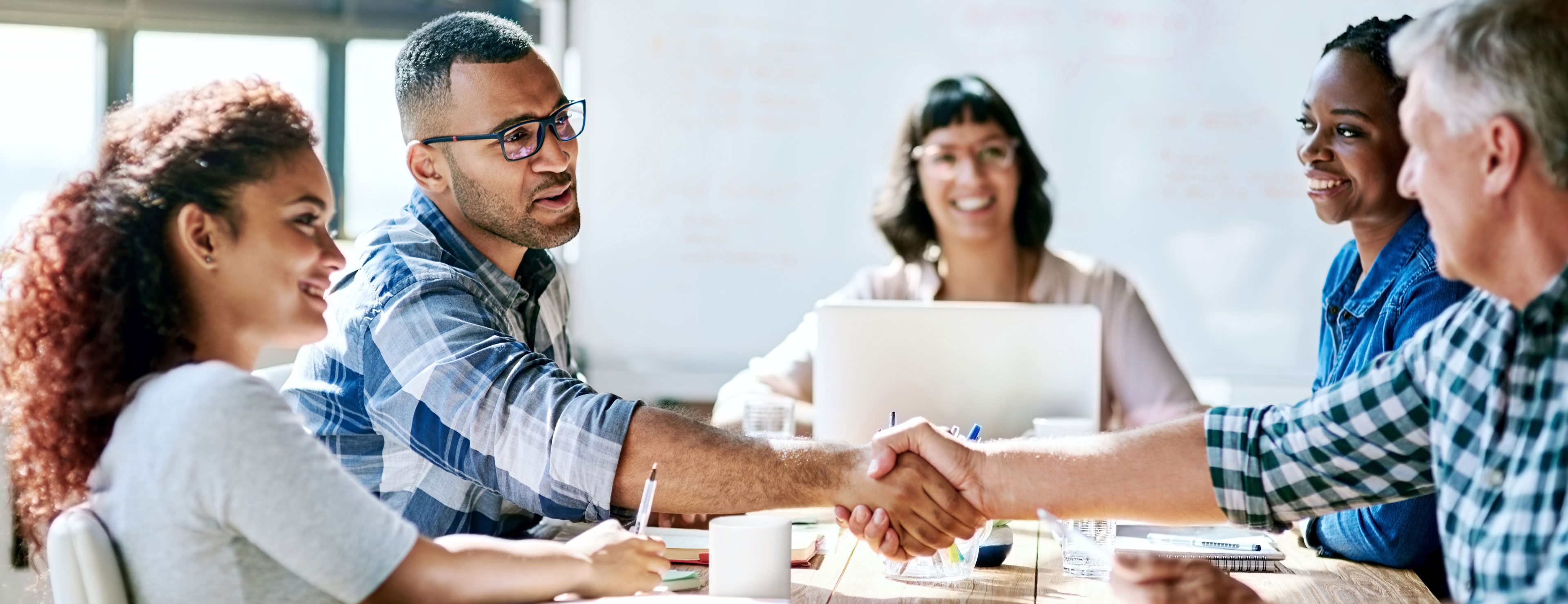 Five people sitting at an office desk, two people are shaking hands